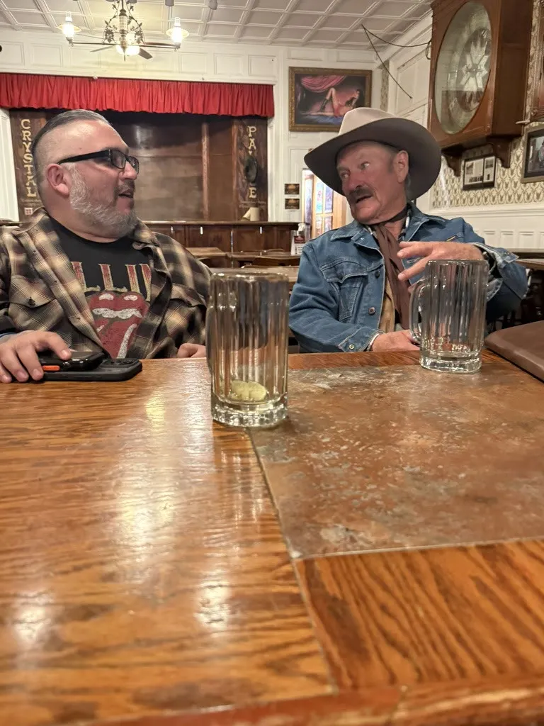 Bear interviewing a man in a cowboy hat at a saloon table in Tombstone, Arizona